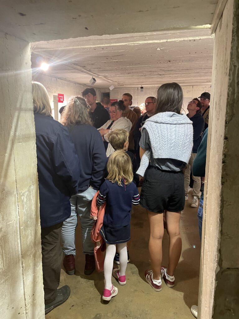 Visiteurs de dos dans une soute à munitions, écoutant le guide.