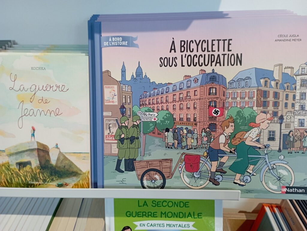 Deux livres jeunesses sur une étagère ; a gauche "La guerre de Jeanne" et à droite "A bicyclette sous l'Occupation". 